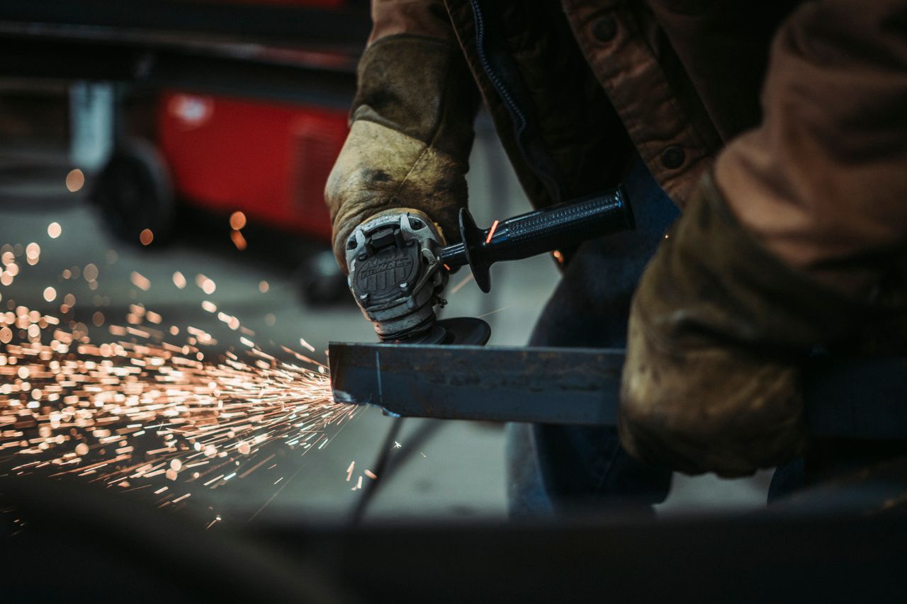 services-03 A skilled worker using an angle grinder sparks fly as they cut metal in a workshop.