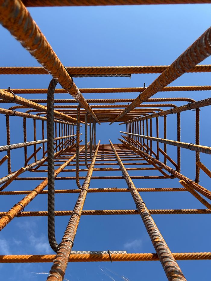 gallery-3 Perspective view of rusted steel rebar forming a tower against a clear blue sky.