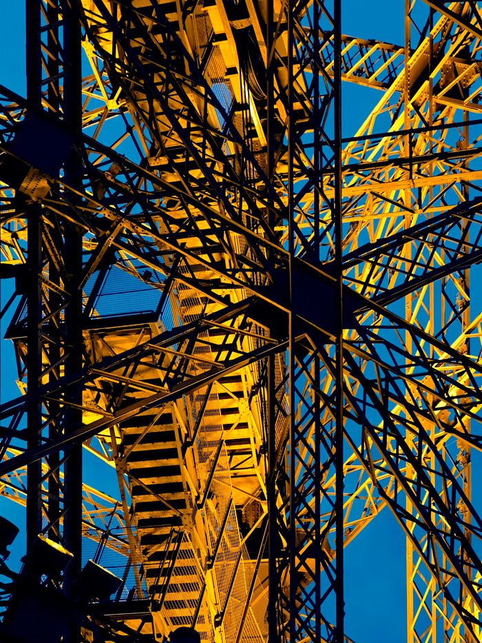 why-choose-us Close-up of industrial steel beams illuminated in gold, set against a clear blue sky.
