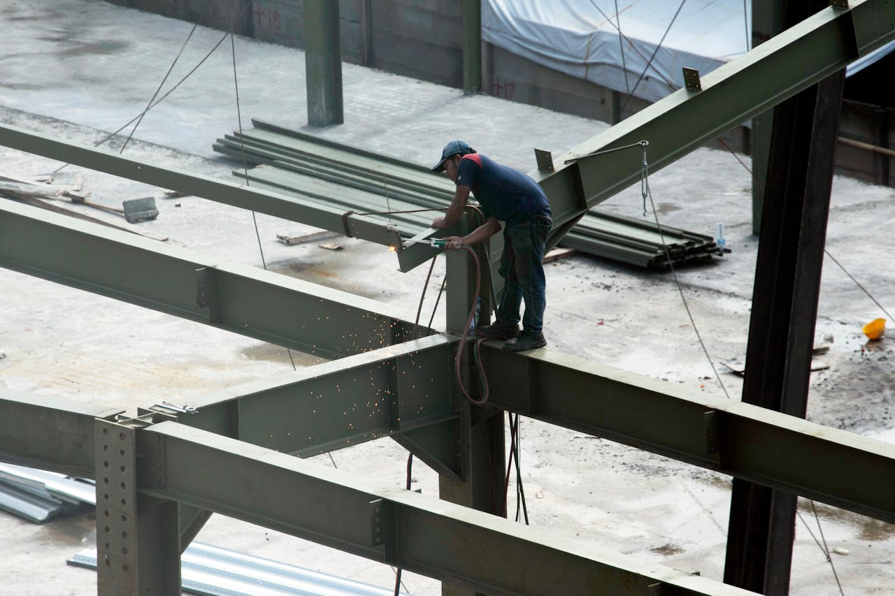 hero-img-02 A construction worker welding steel beams on a high-rise construction site. Sparks fly as the worker welds.
